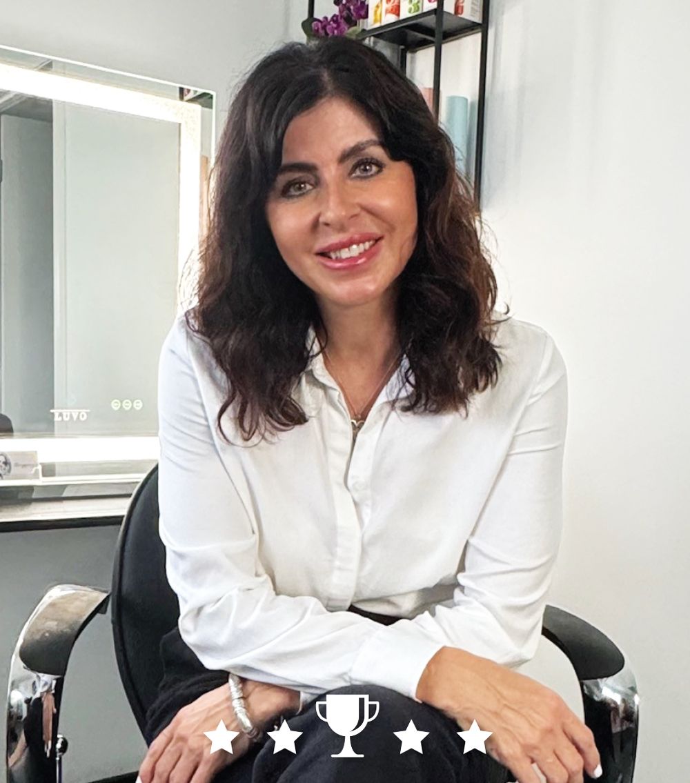 A woman is sitting in a chair with her arms crossed and smiling.