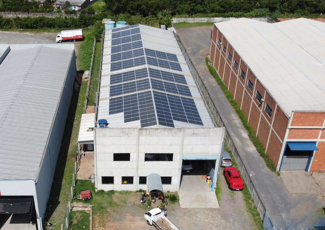 Vista aérea de um armazém com painéis solares no telhado, ao lado de edifícios industriais vizinhos.