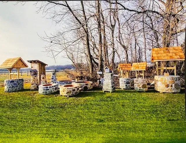 A row of wells in a grassy field with trees in the background