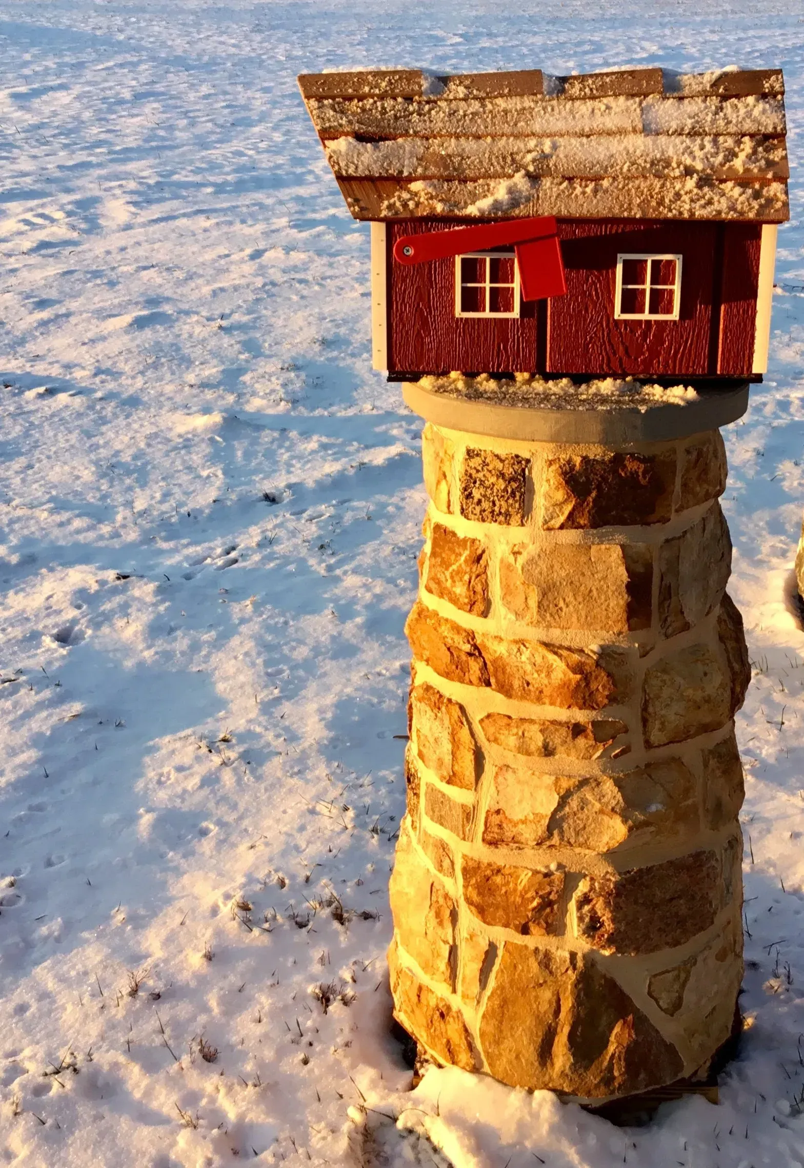 A small red house is sitting on top of a stone pillar in the snow.