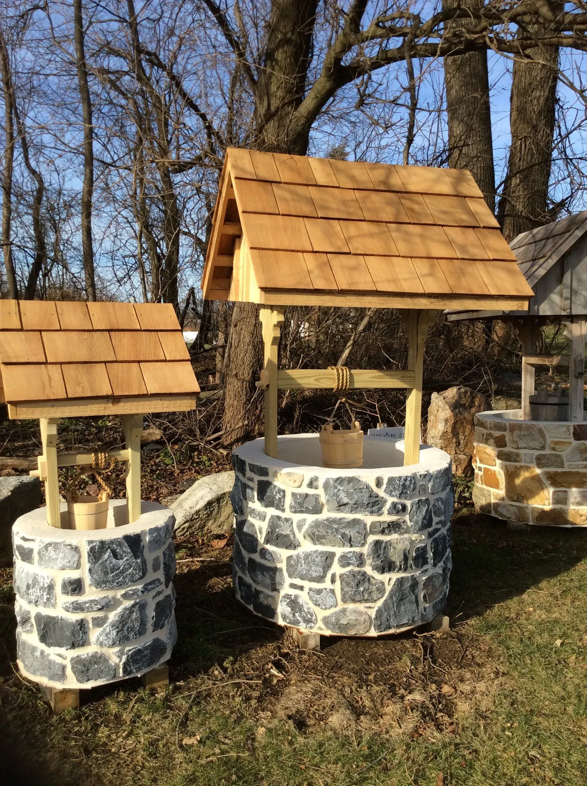 A stone wishing well with a wooden roof is sitting in the grass.