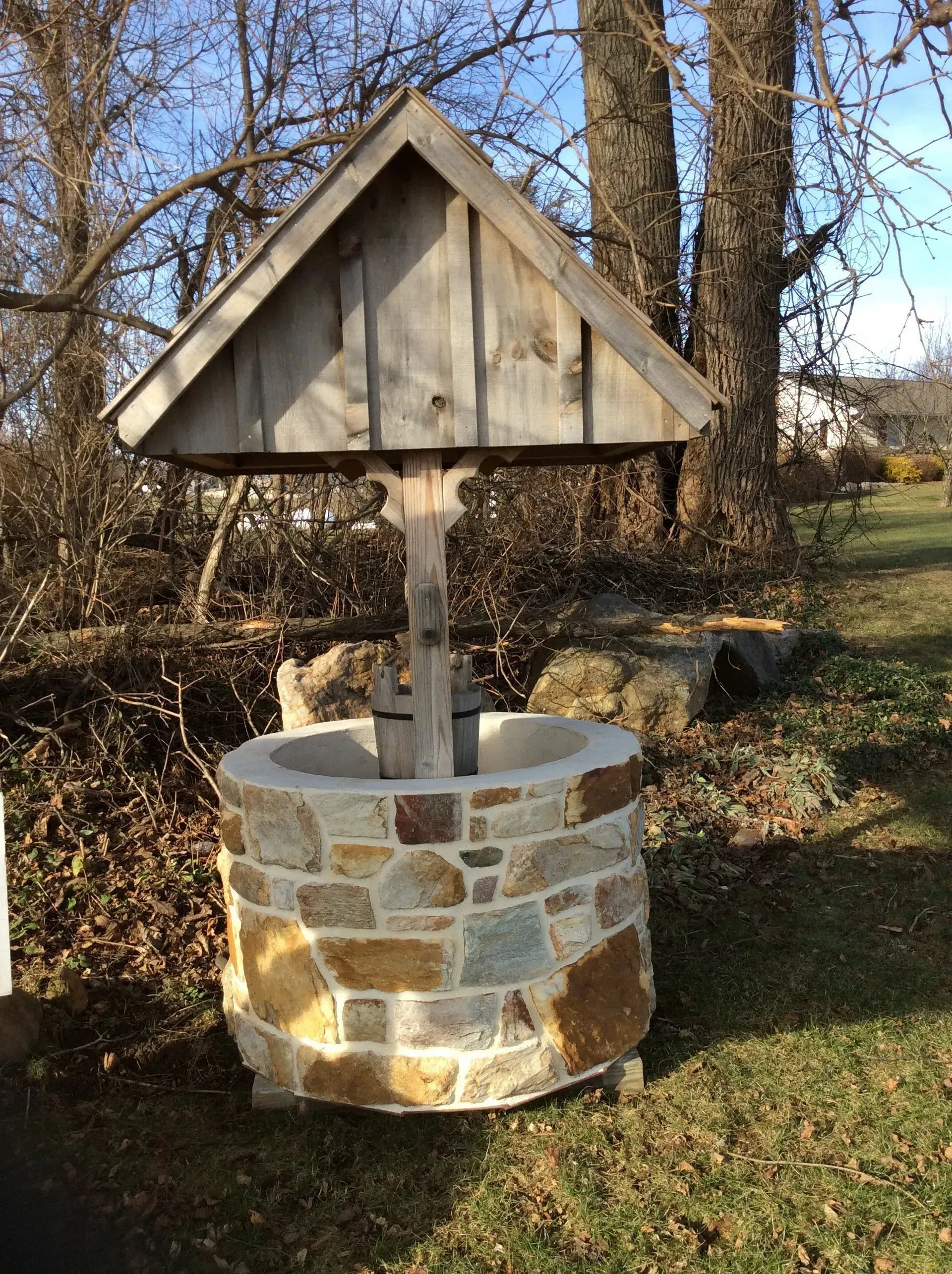 A stone well with a wooden roof is sitting in the grass.