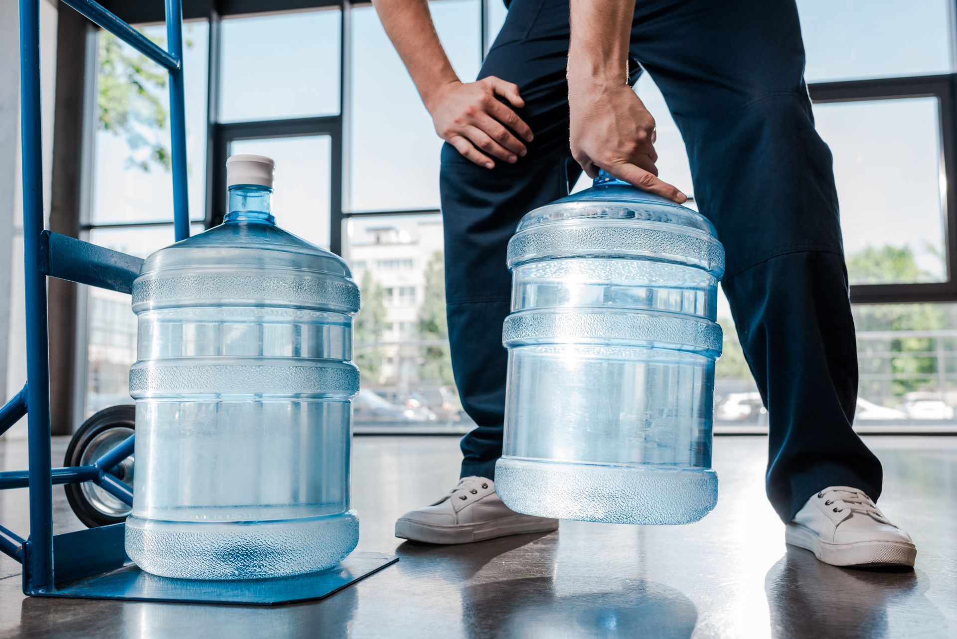 cropped view of delivery man holding heavy bottle with water near hand truck cropped view of delivery man holding heavy bottle with water near hand truck