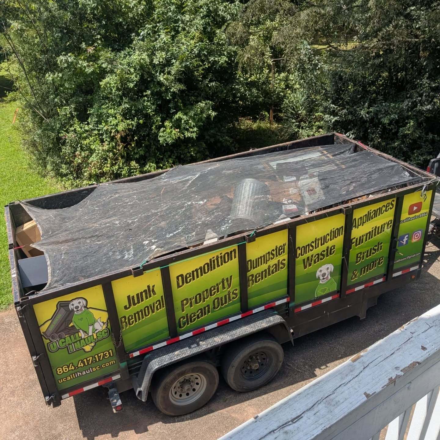 Dumpster trailer with business signage; tarp covers debris. Parked outdoors.