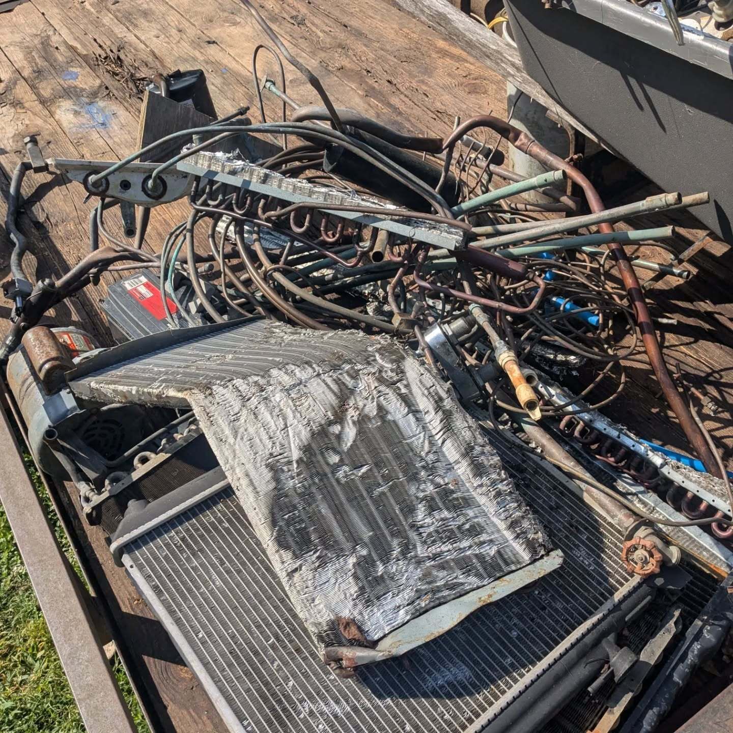 Pile of scrap metal on a wooden trailer bed, including radiators, tubes, and wires.
