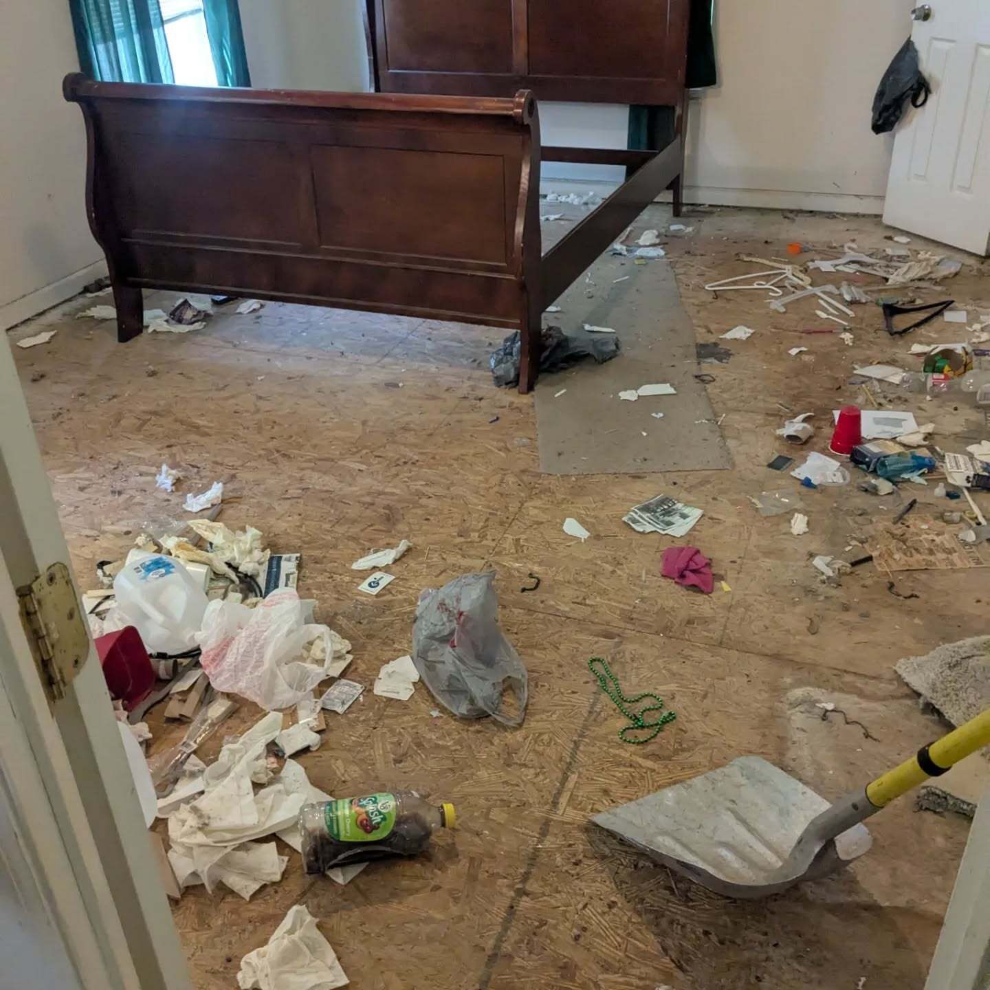 A cluttered room with a bed, trash on the floor, and a shovel.