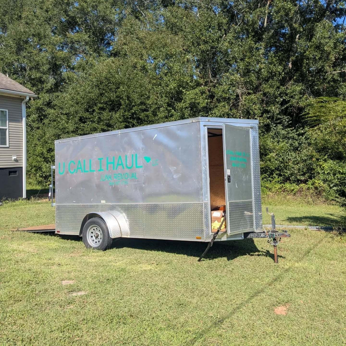 Silver U-Haul trailer with open door, parked on a grassy yard.