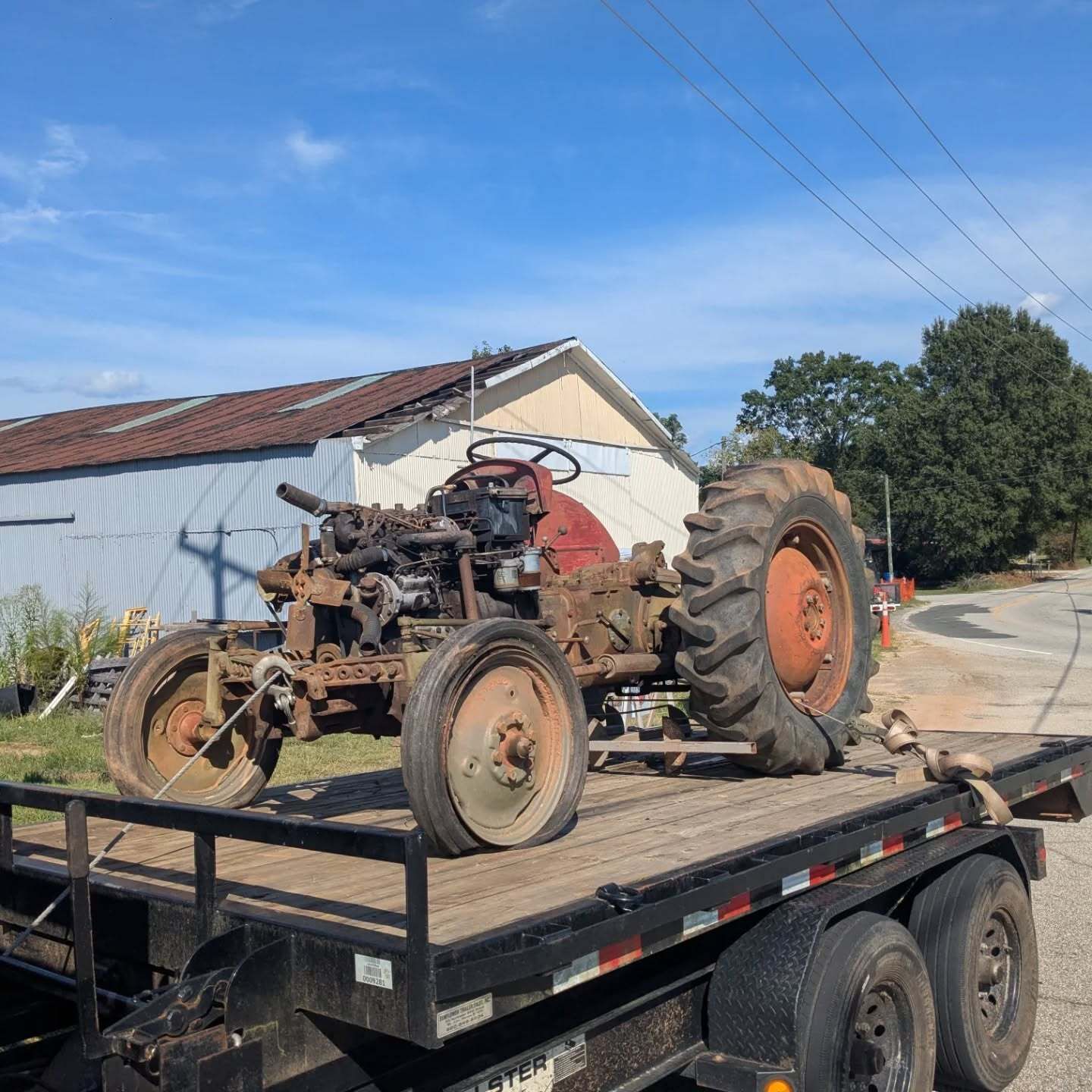 Old, rusty tractor on a trailer, under a bright blue sky.