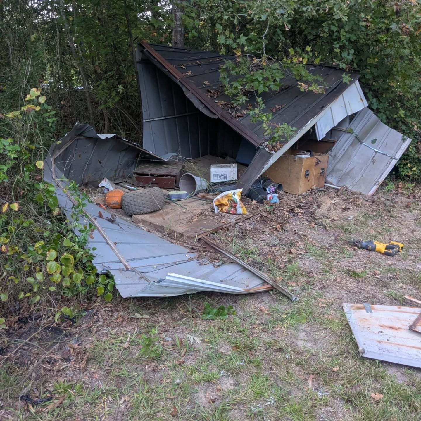 Collapsed metal shed with debris scattered on the ground near vegetation.
