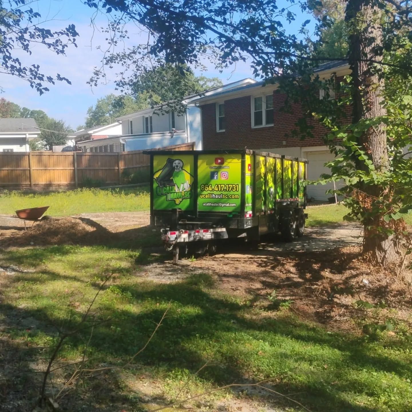 A dumpster trailer on a lawn near a house. Green and yellow colors are prominent.