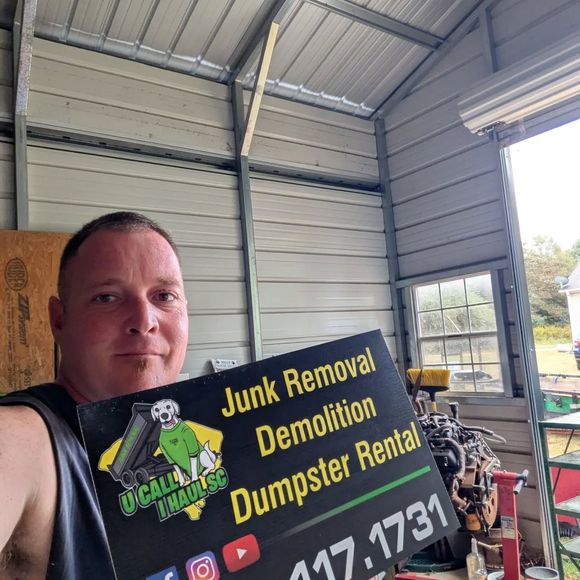 Man holding sign for junk removal, demolition, and dumpster rental inside a shed.