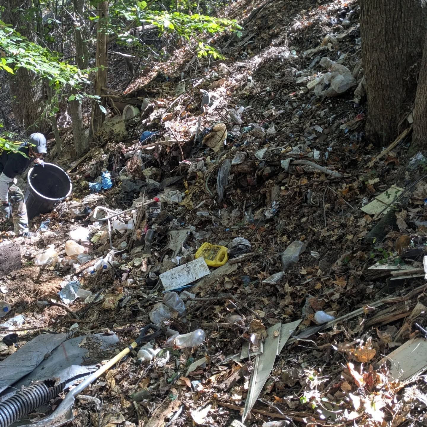 Trash piled on a wooded hillside; includes plastic, metal, and other debris.
