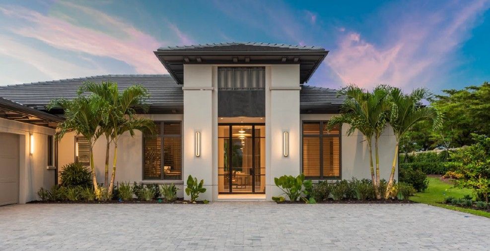 Modern white house with dark trim, palm trees, and a paved driveway.