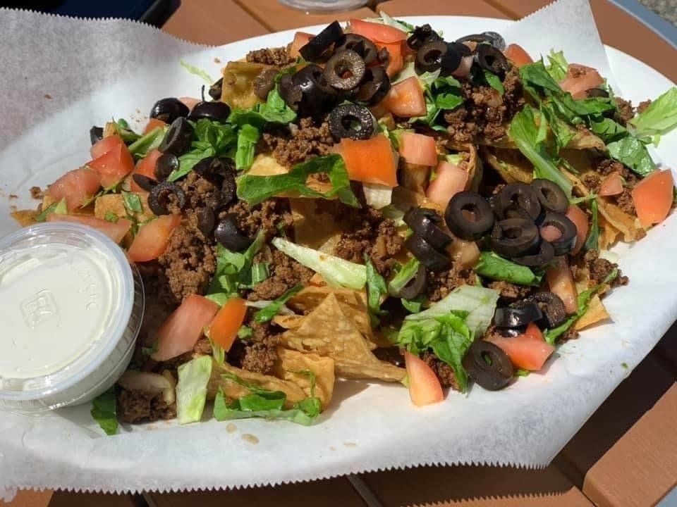 A plate of beef nachos topped with lettuce, tomatoes, and sliced black olives, served with a side of sour cream.