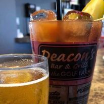 A tall glass containing a Bloody Mary with a garnish next to a smaller glass of light-colored beer on a table.