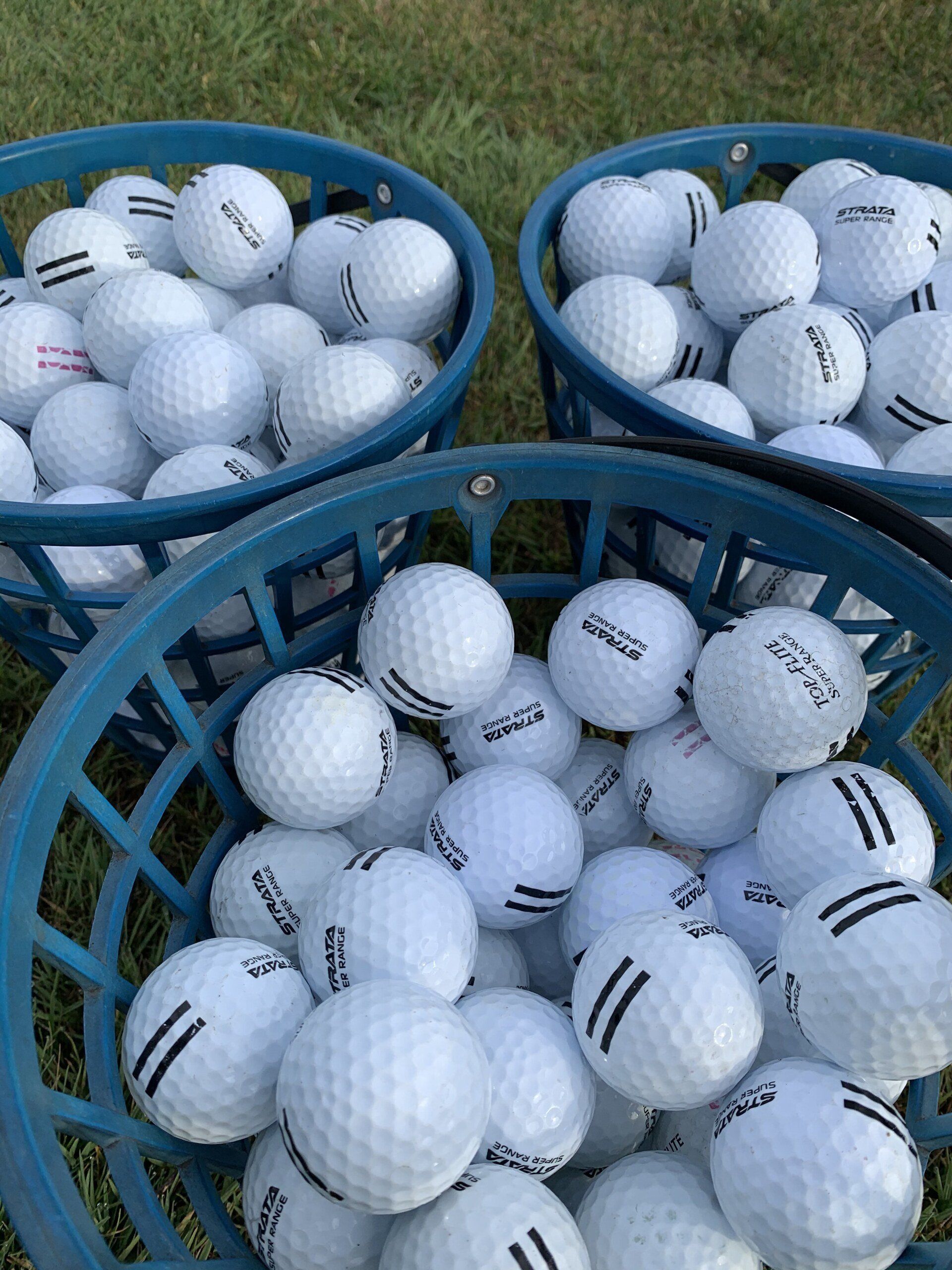 Three blue plastic baskets filled with white golf balls, sitting on green grass.