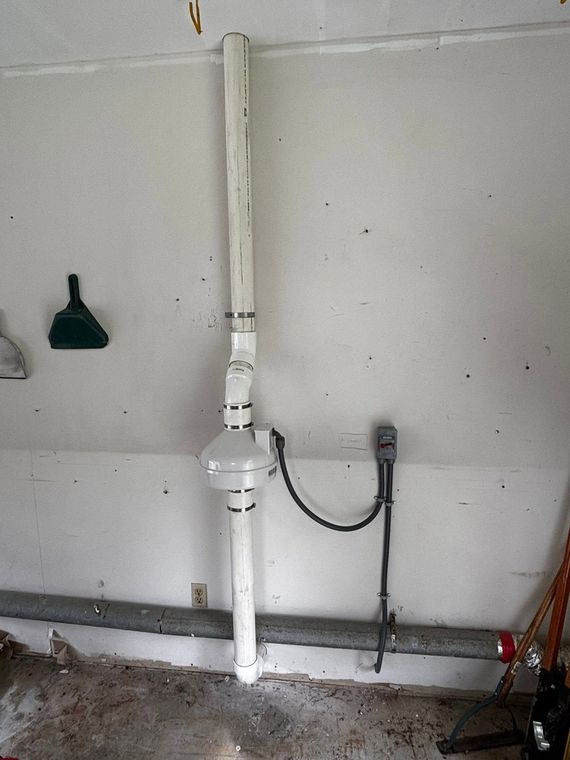 White ceiling-mounted pipe with valve and connected gray conduit on a wall, likely plumbing or utility equipment