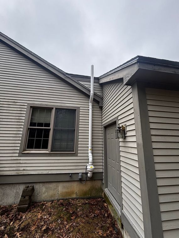 Side view of a gray house exterior with a broken window and a white downspout between two walls.