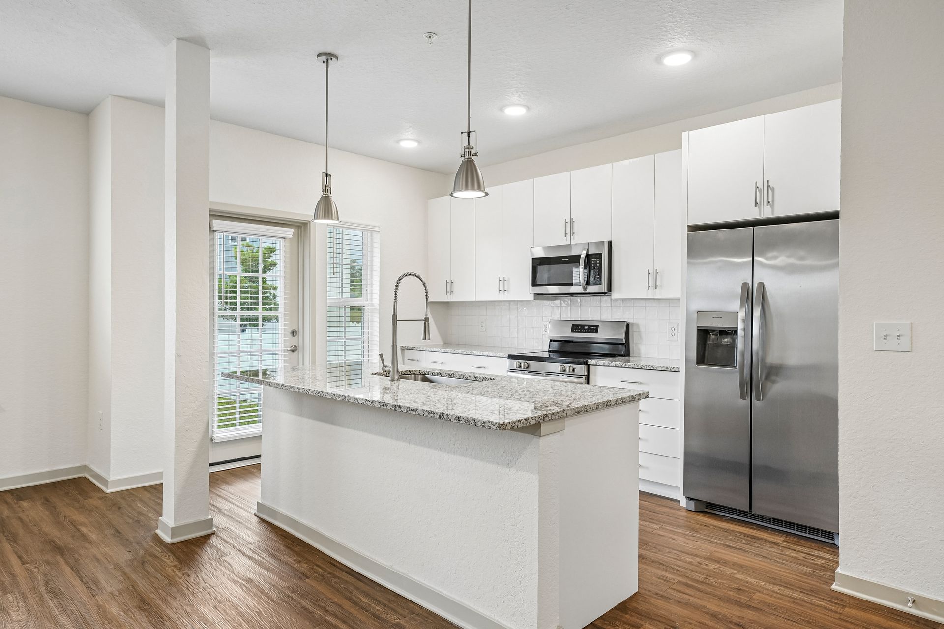 Bright modern kitchen with white cabinets, granite island, stainless steel appliances, and wood floors