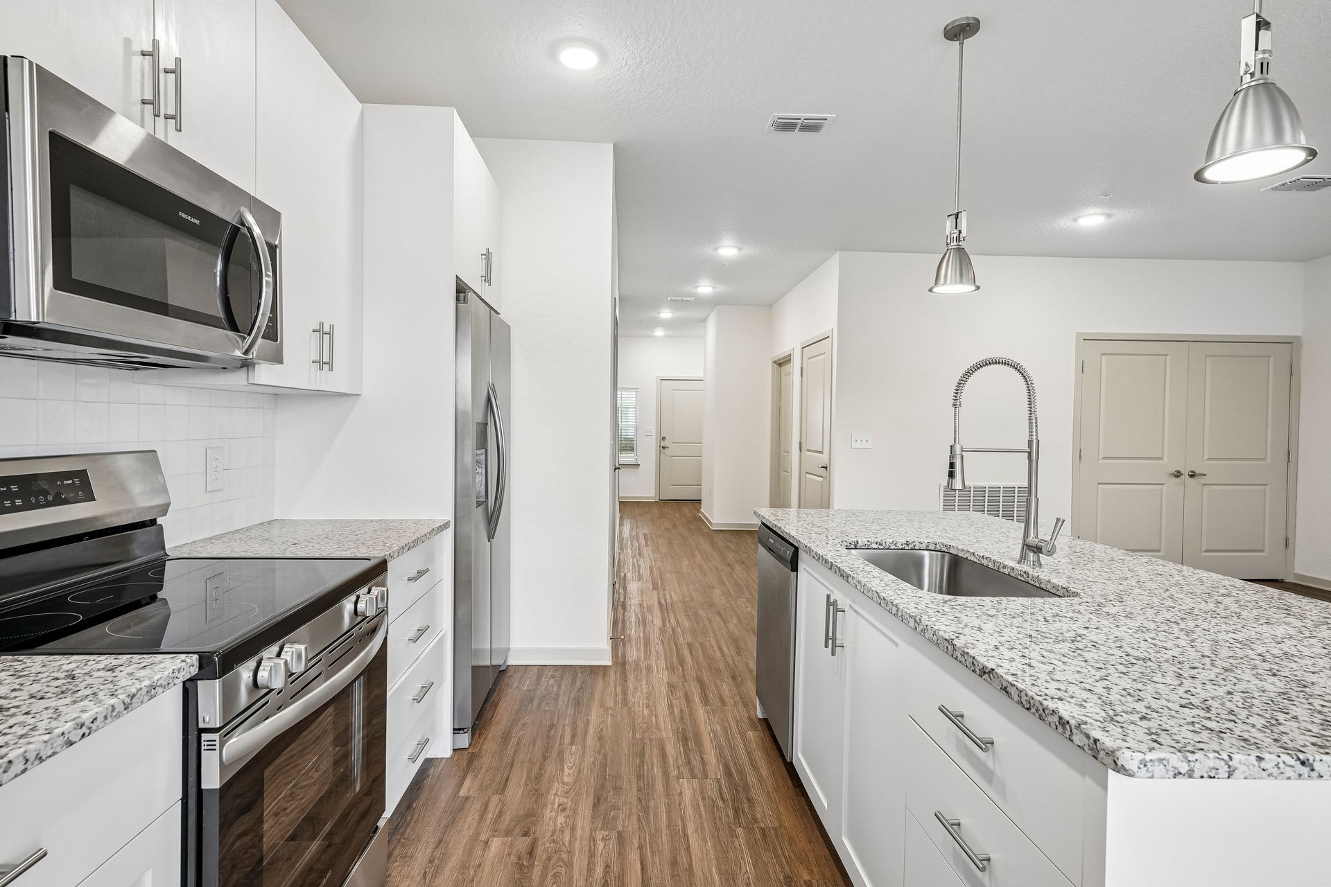 Bright white kitchen with stainless steel appliances, granite counters, island sink, and wood-look flooring