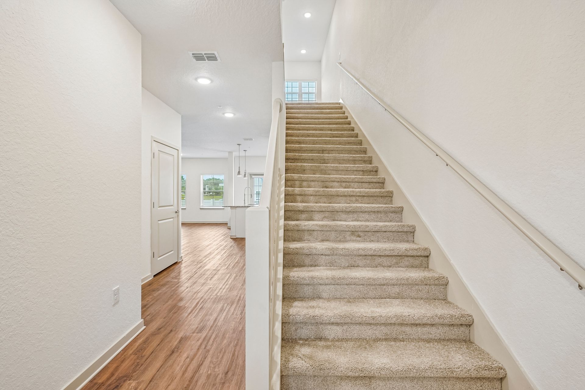 Bright hallway with carpeted staircase, white walls, wood floor, and landing window above stairs