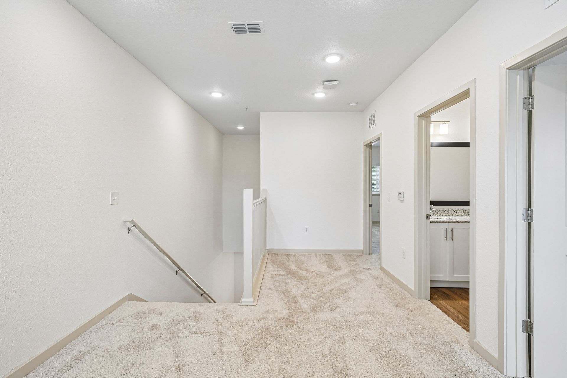Bright upstairs hallway with carpet, stair railing, recessed lights, and open doorways to a closet and bathroom