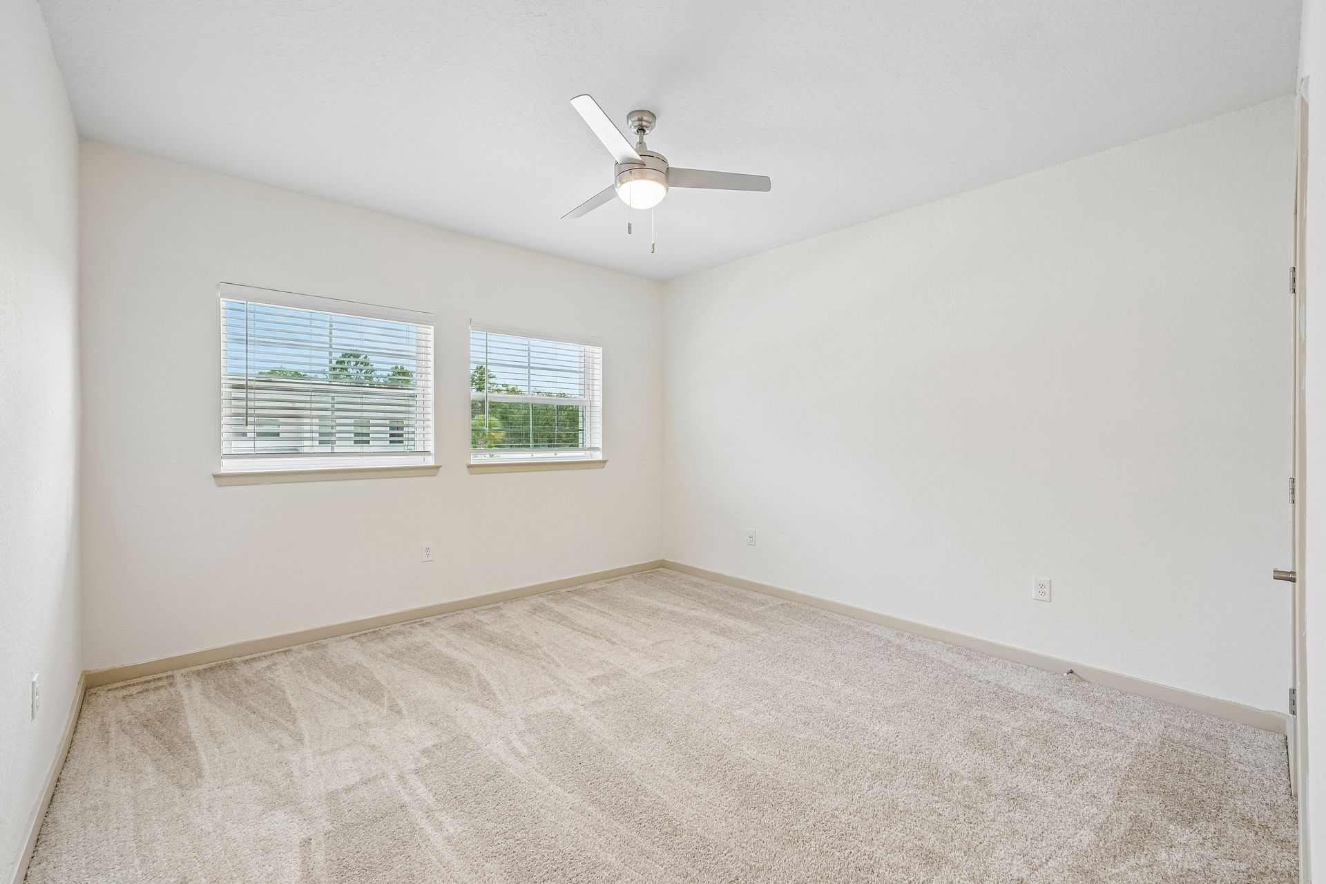 Empty white carpeted bedroom with two windows and a ceiling fan