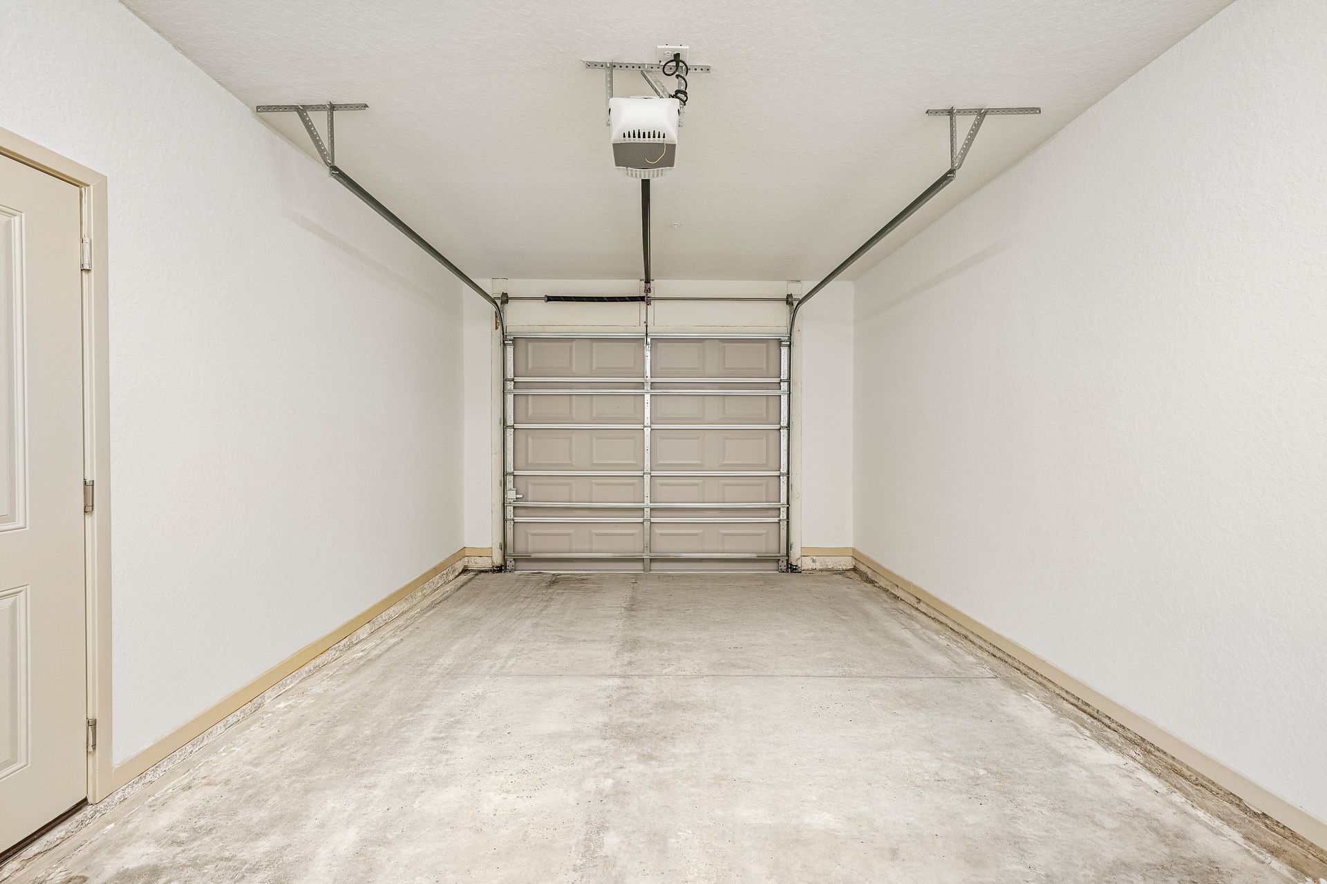 Empty white garage with a closed metal overhead door and concrete floor