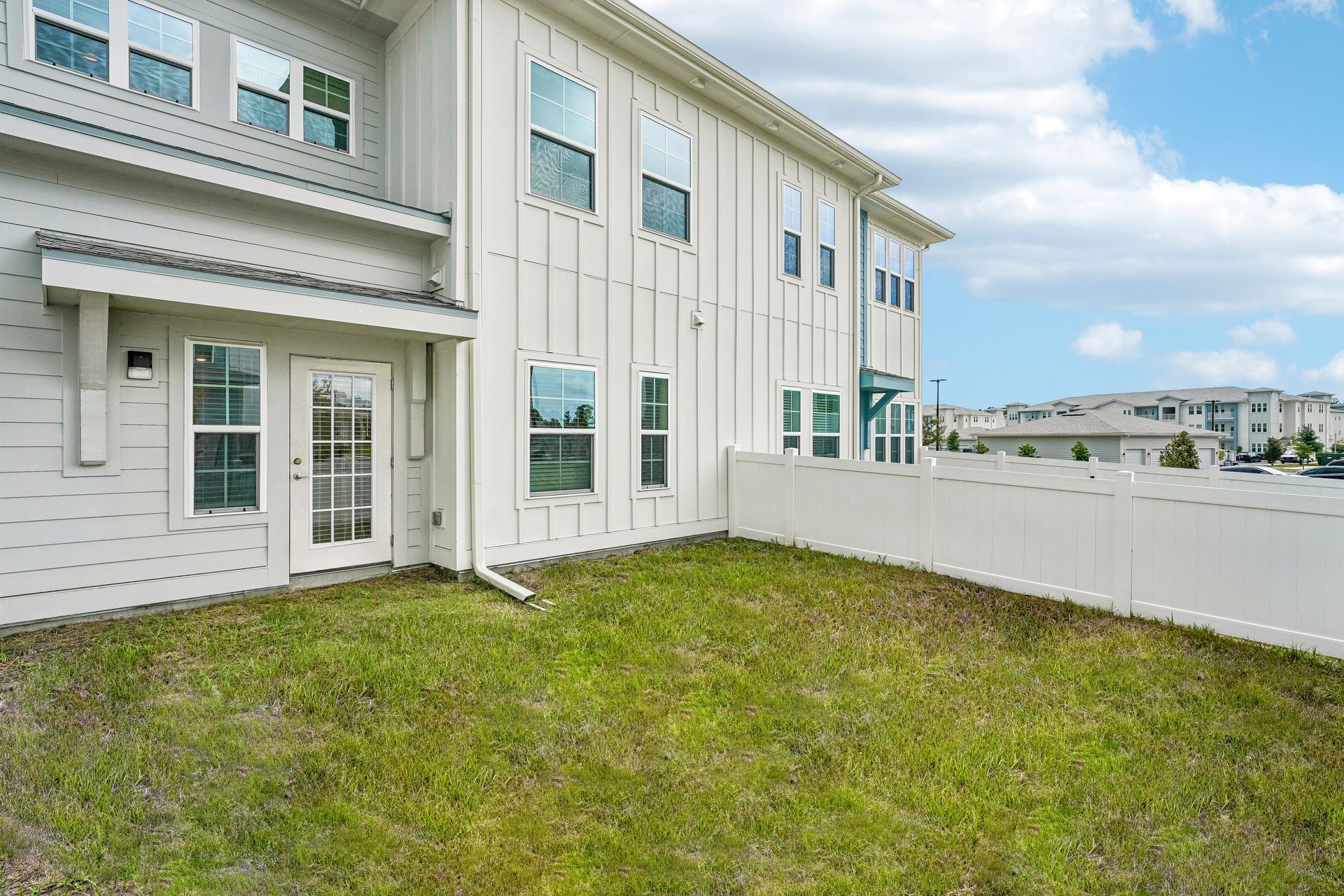 Backyard lawn beside a white two-story house with large windows and a patio fence