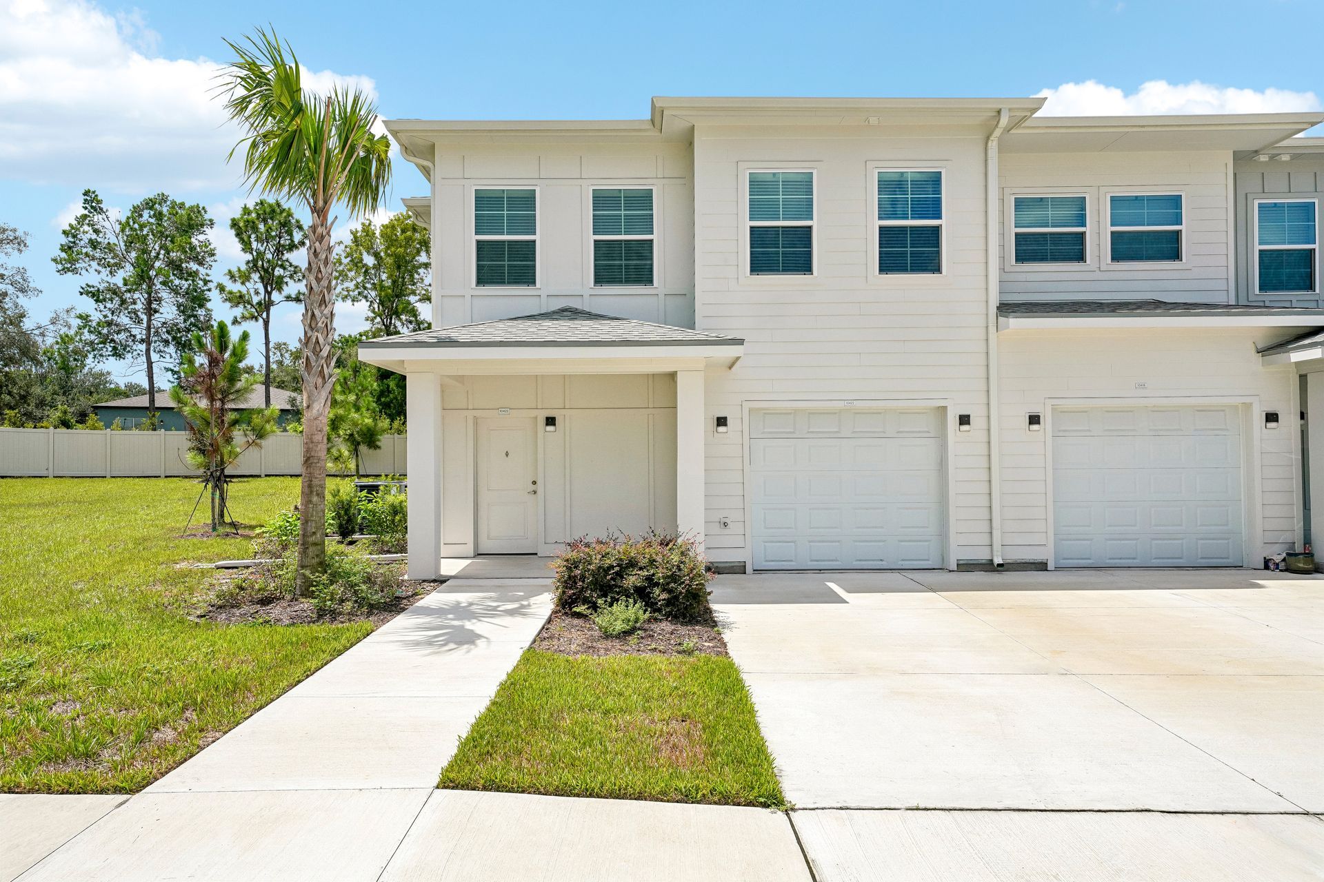 White two-story townhouse with garage and driveway under a bright blue sky