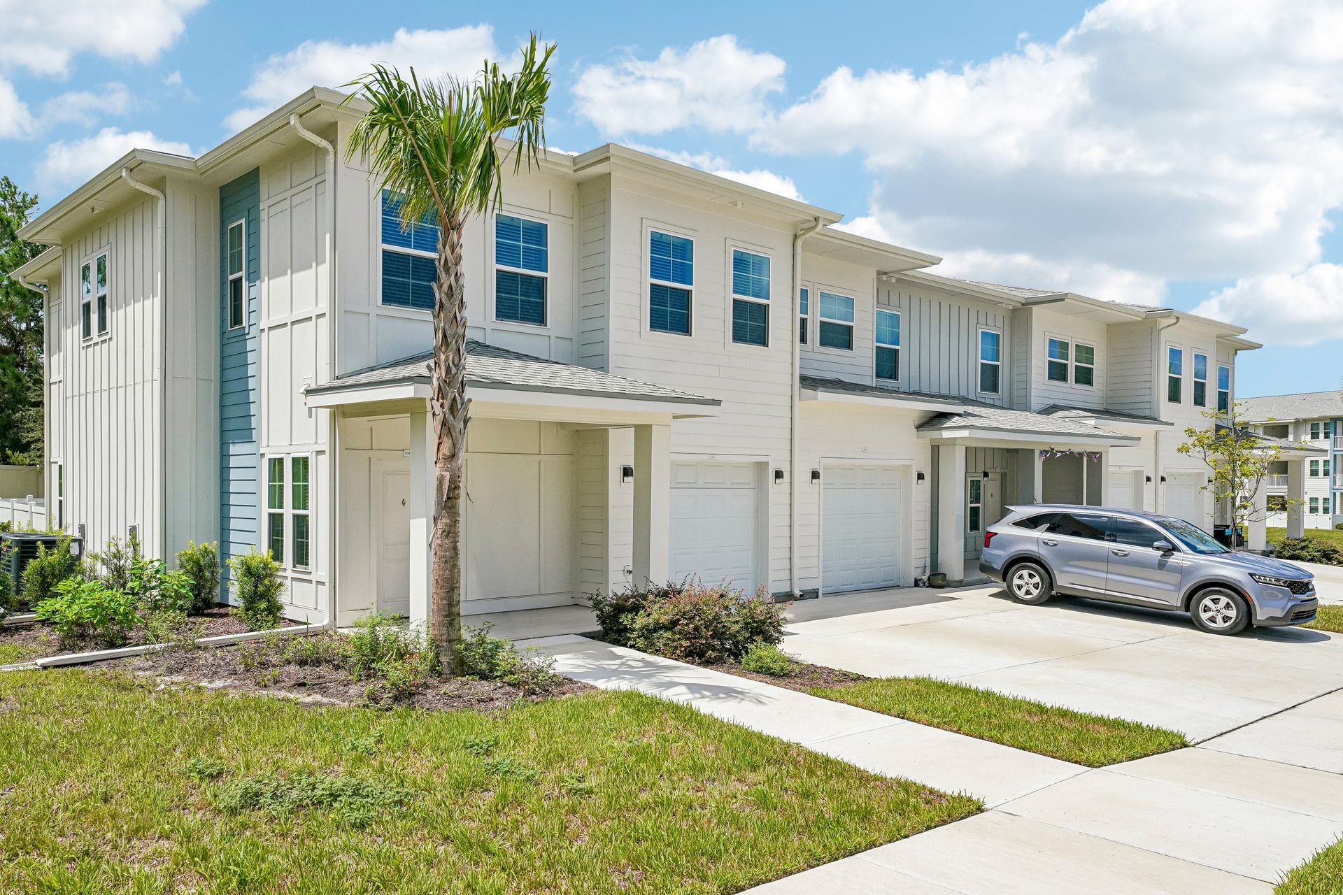 Row of beige townhomes with garages and a parked silver car on a sunny day
