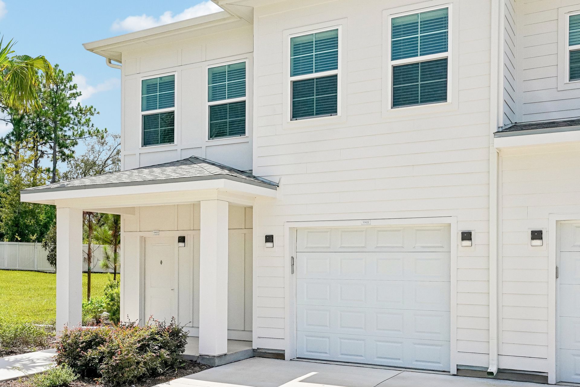 White two-story townhouse exterior with a covered entry, garage, and teal-trimmed windows