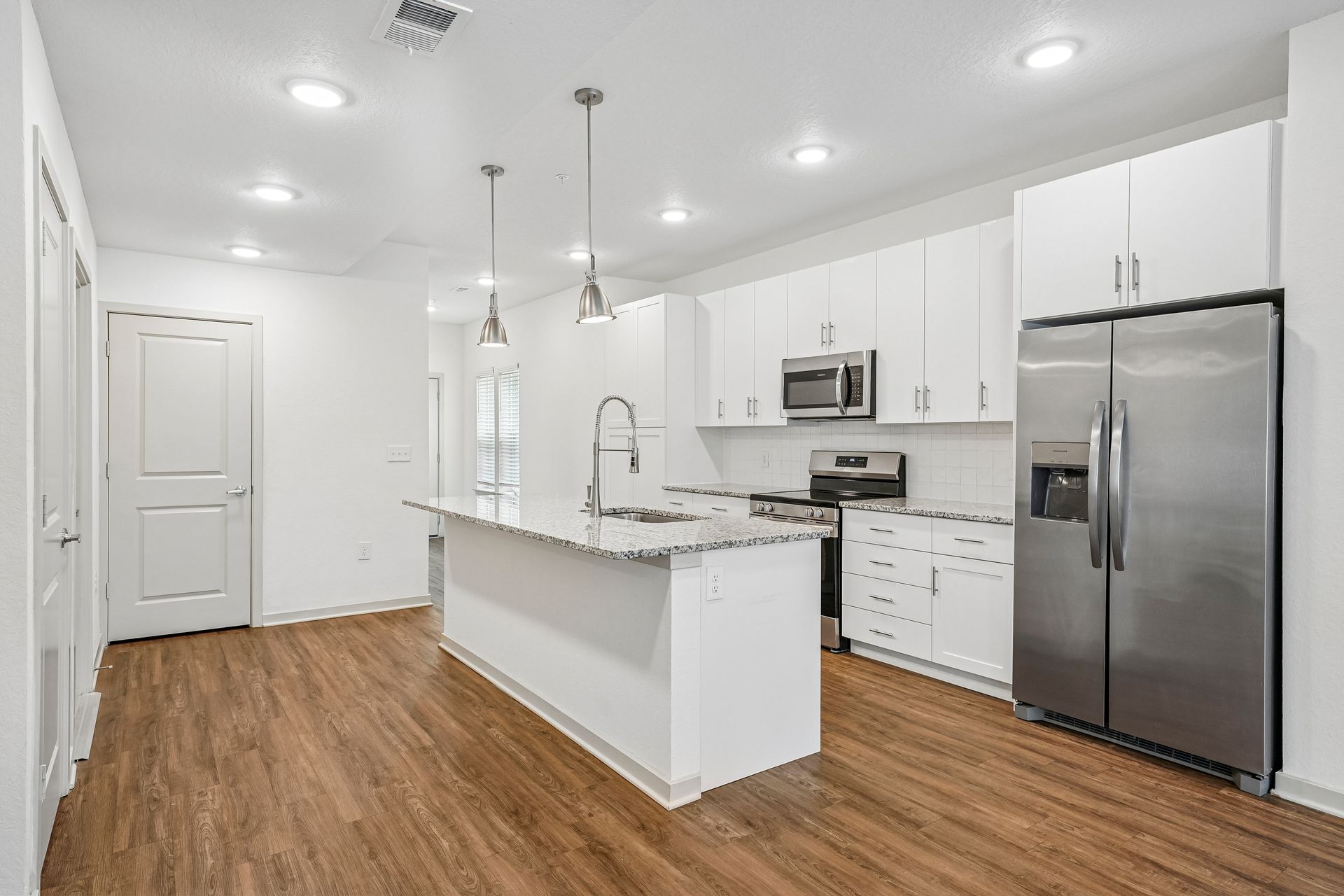 Bright modern white kitchen with stainless steel appliances, island, and wood floors