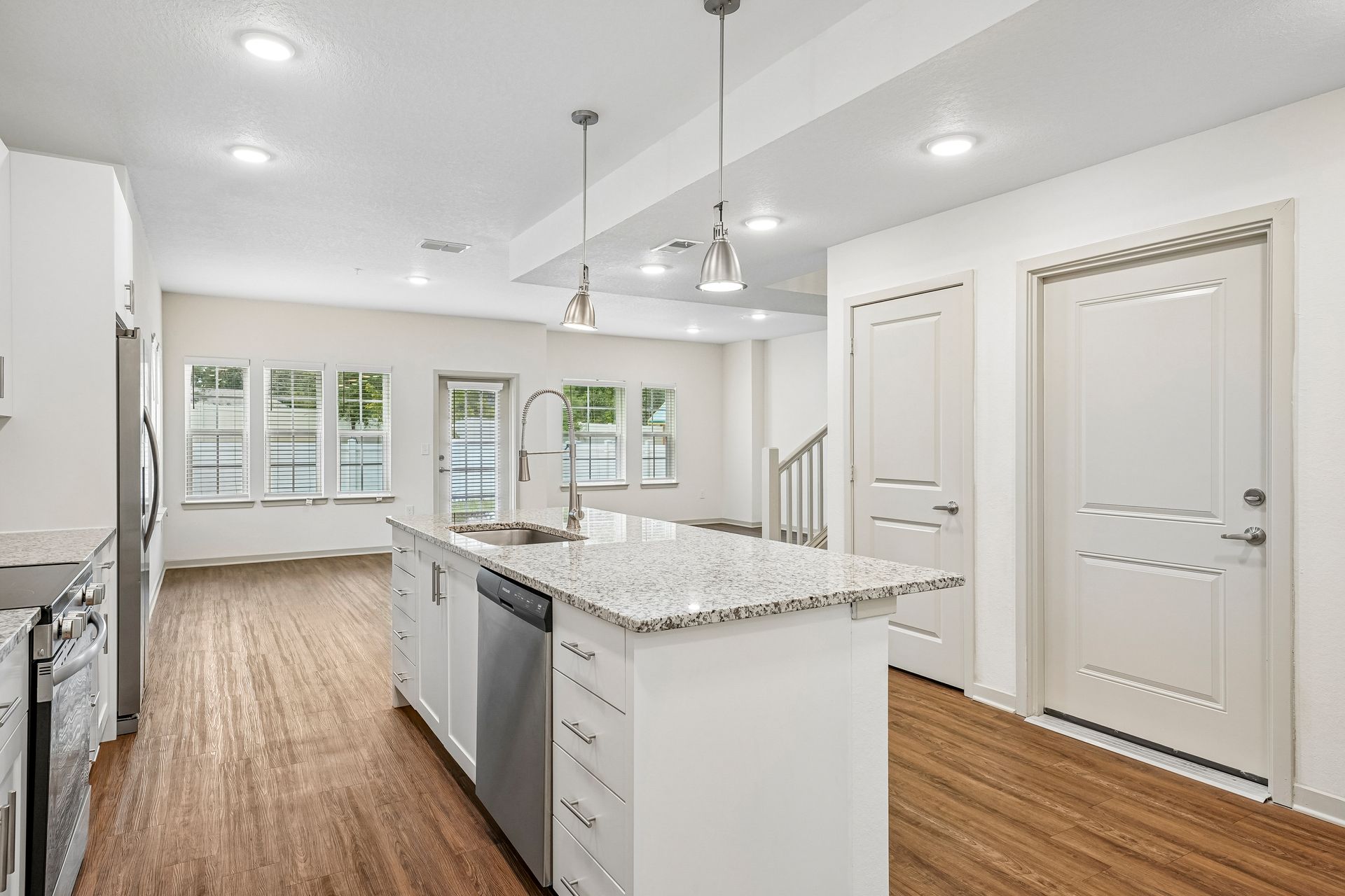 Bright modern kitchen with white cabinets, island, stainless appliances, and wood floors