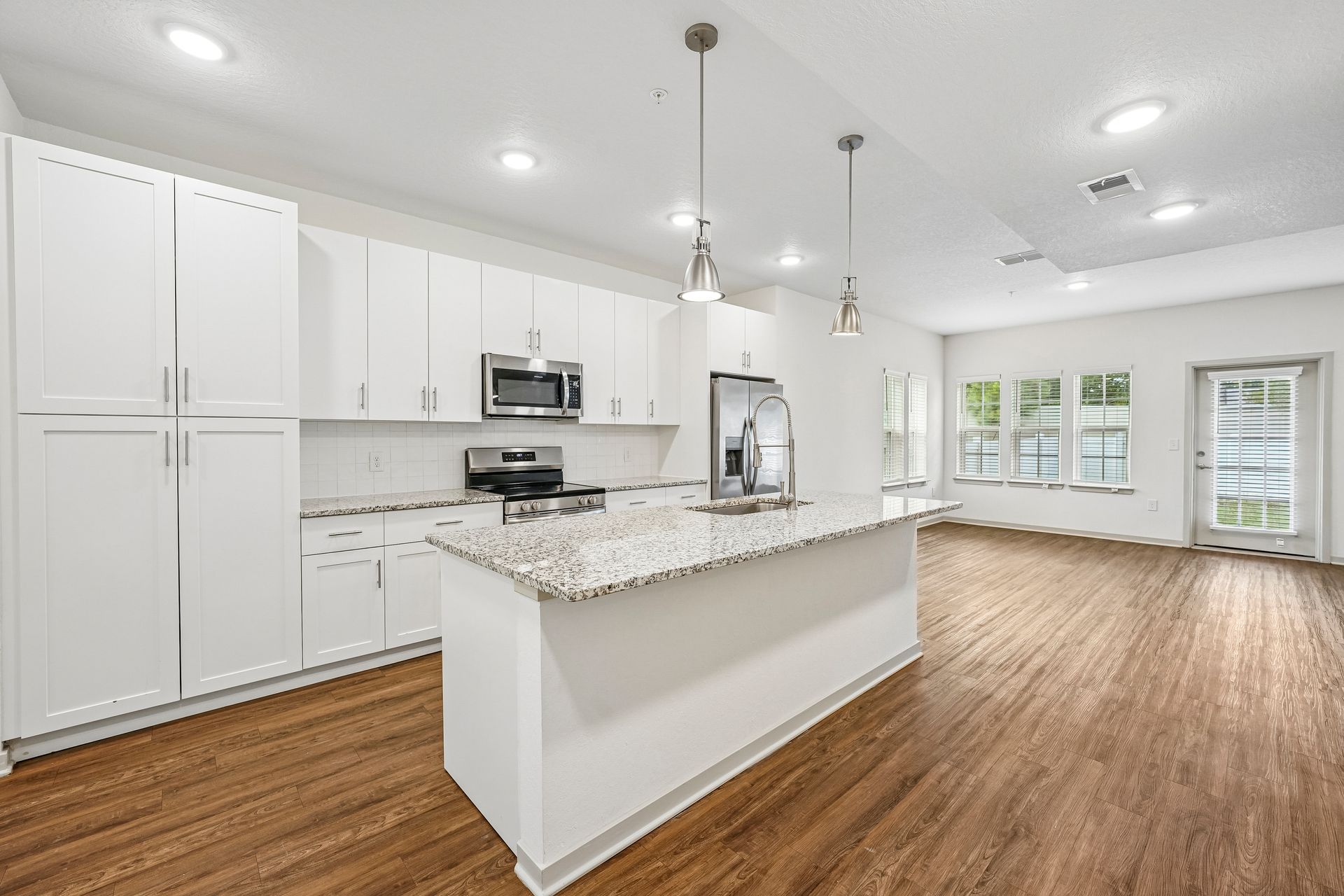 Bright modern white kitchen with island, stainless appliances, granite counters, and hardwood floors