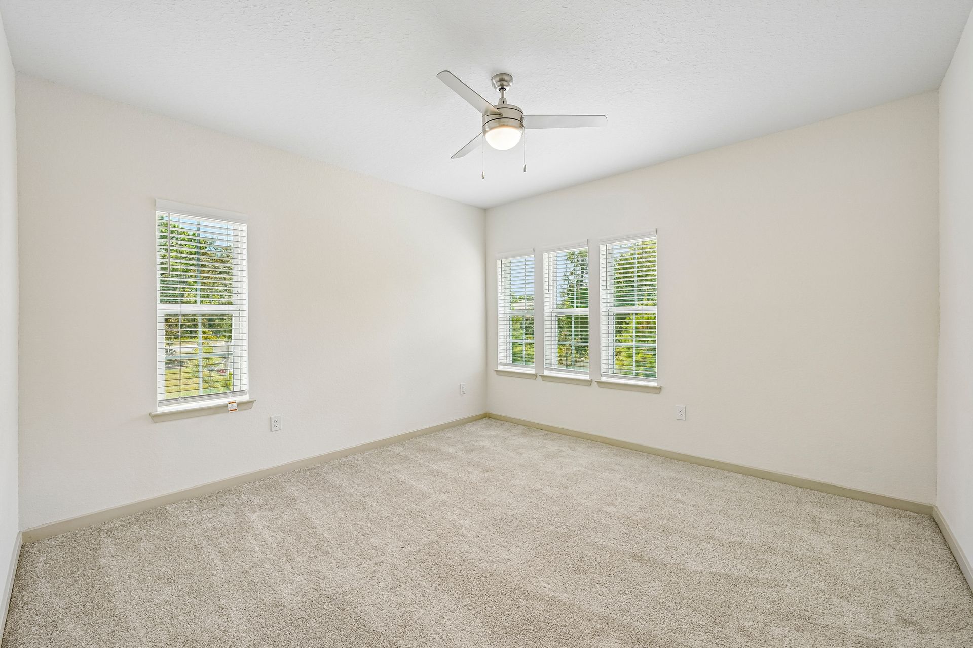 Empty carpeted bedroom with white walls, two windows, and a ceiling fan