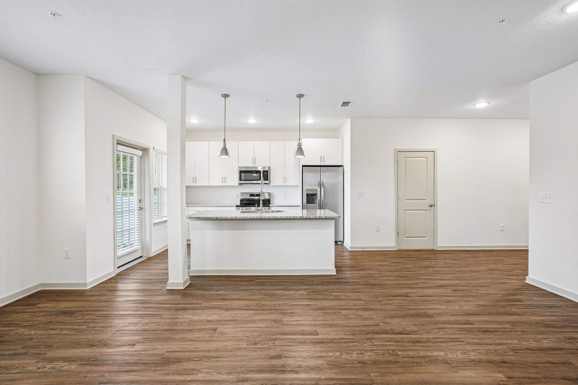Bright empty open-plan kitchen and living room with white walls and wood floors