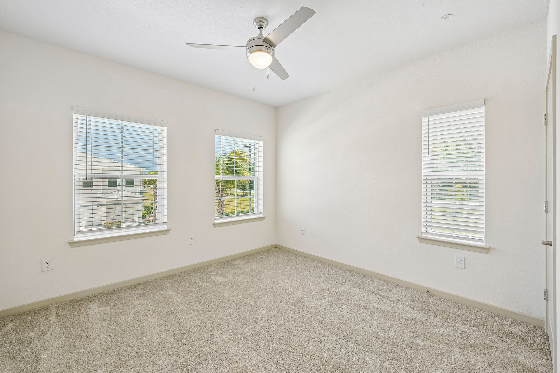 Empty white bedroom with carpet, three windows, and a ceiling fan
