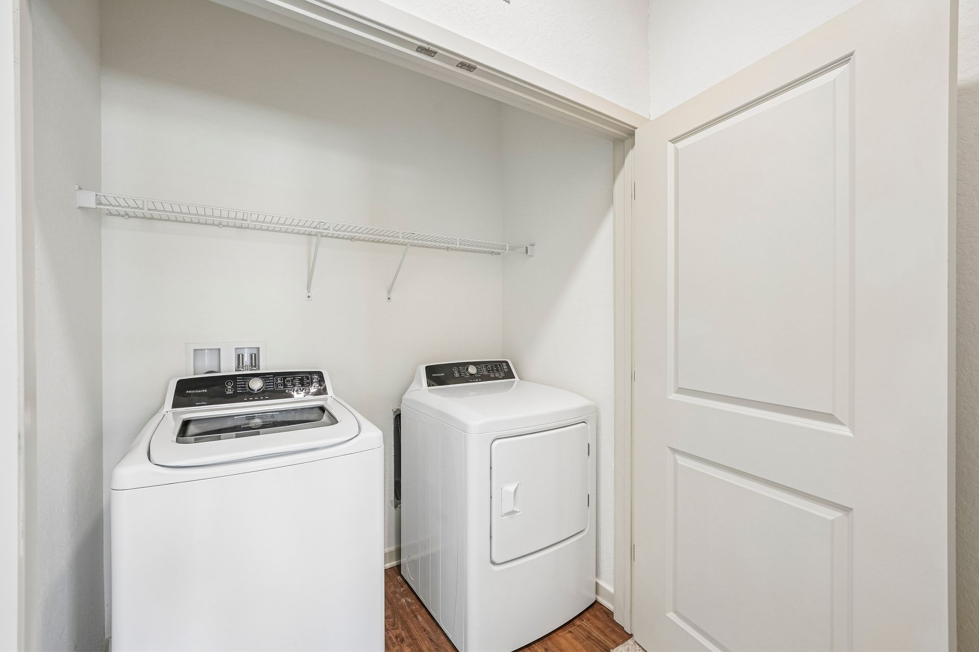 Laundry closet with a white washer, dryer, and hanging rod under a shelf