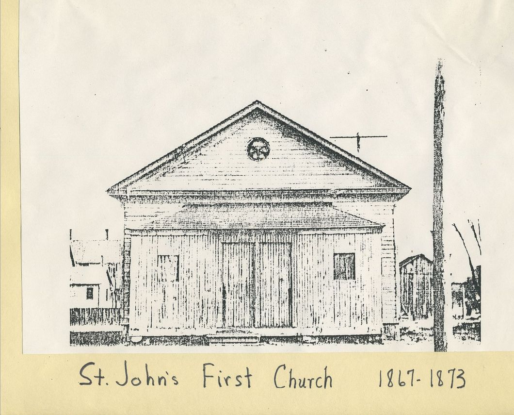 St. John's First Church, circa 1861-1873. A simple, wood-paneled church with a gabled roof and a small circular window.