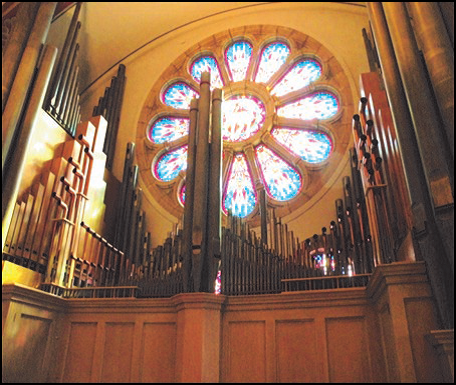 Pipe organ in front of a stained glass window, inside a church.