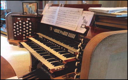 Pipe organ console with keyboards, stops, and sheet music in a church setting.