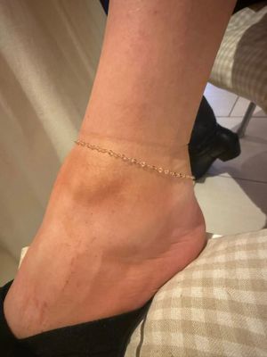 Close-up of a bare ankle wearing a delicate gold anklet and black high heel.