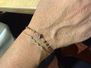 Close-up of a wrist wearing two delicate bracelets, one gold and one wavy silver and blue.