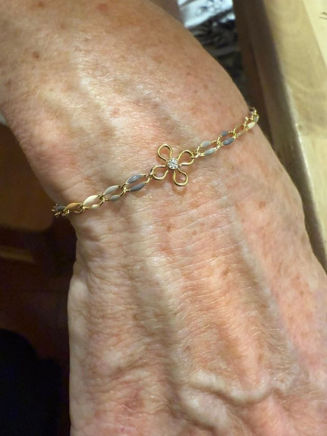 Close-up of a hand wearing a delicate gold bracelet with a small bow charm