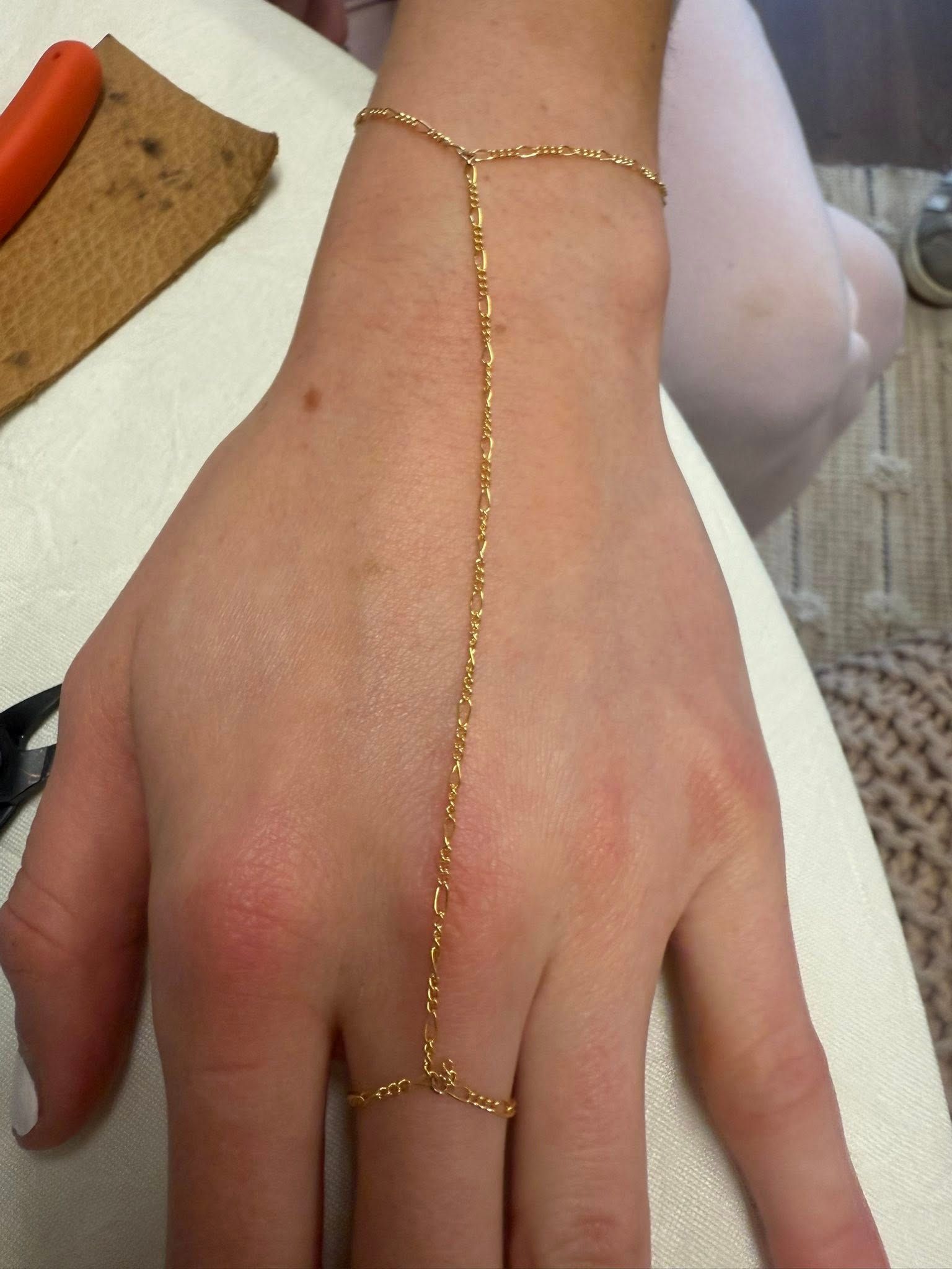 Hand wearing a delicate gold chain hand harness on a white background