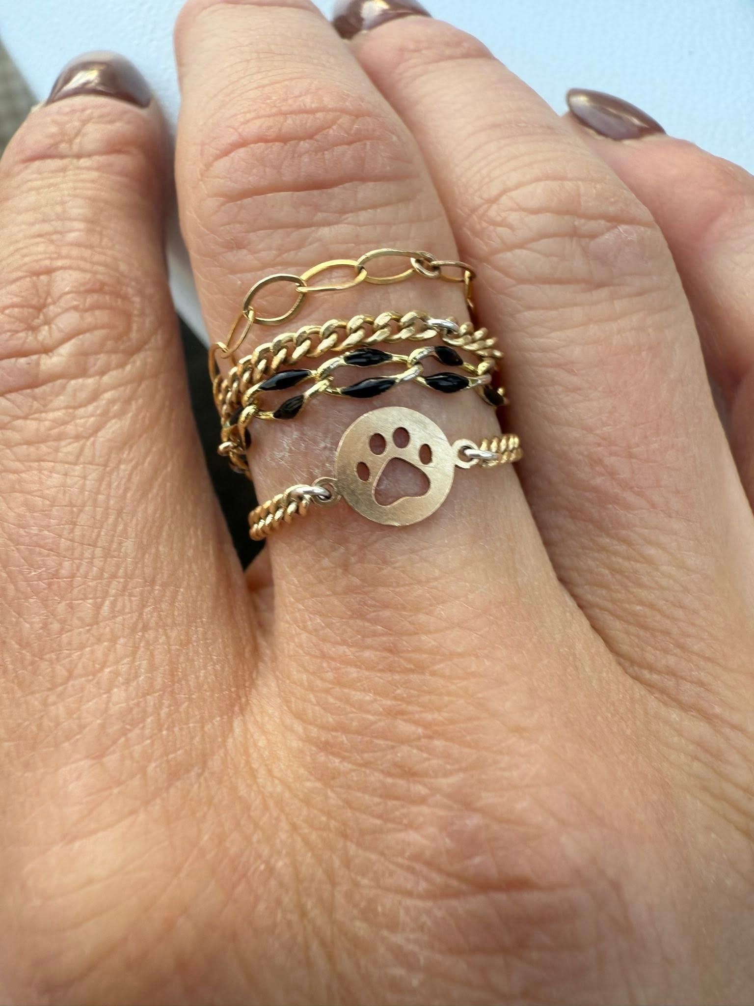 Hand with stacked gold rings, including a chain band and a paw-print charm.