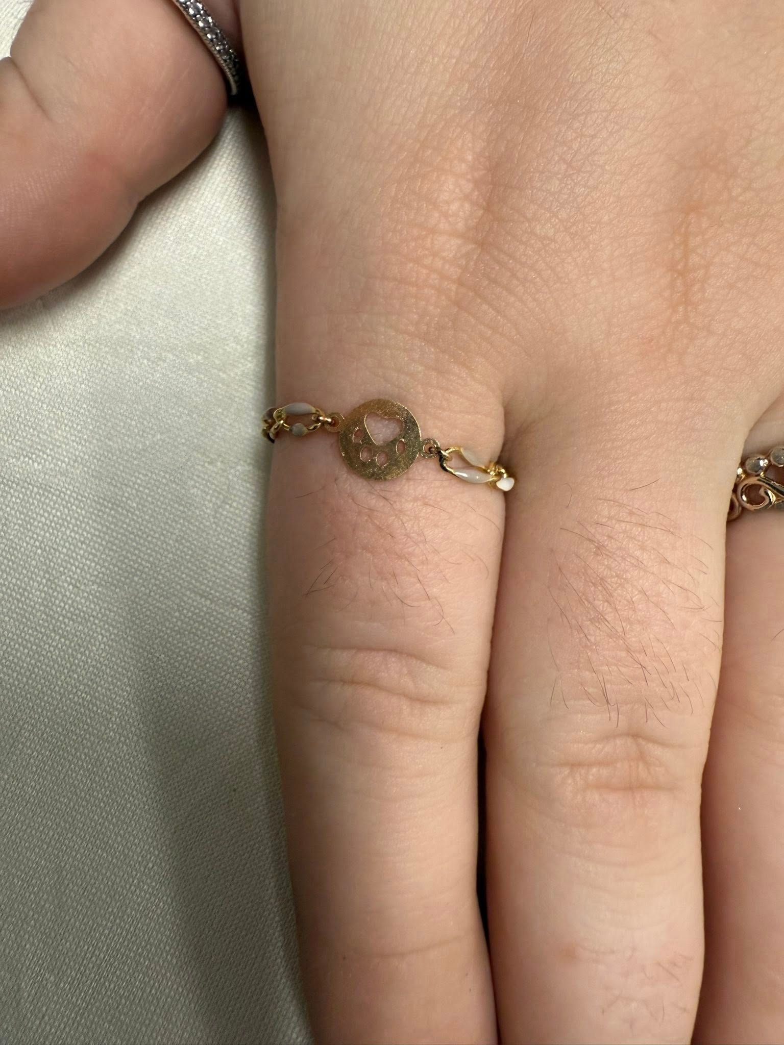 Hand wearing a delicate gold chain ring with a round charm on a light background