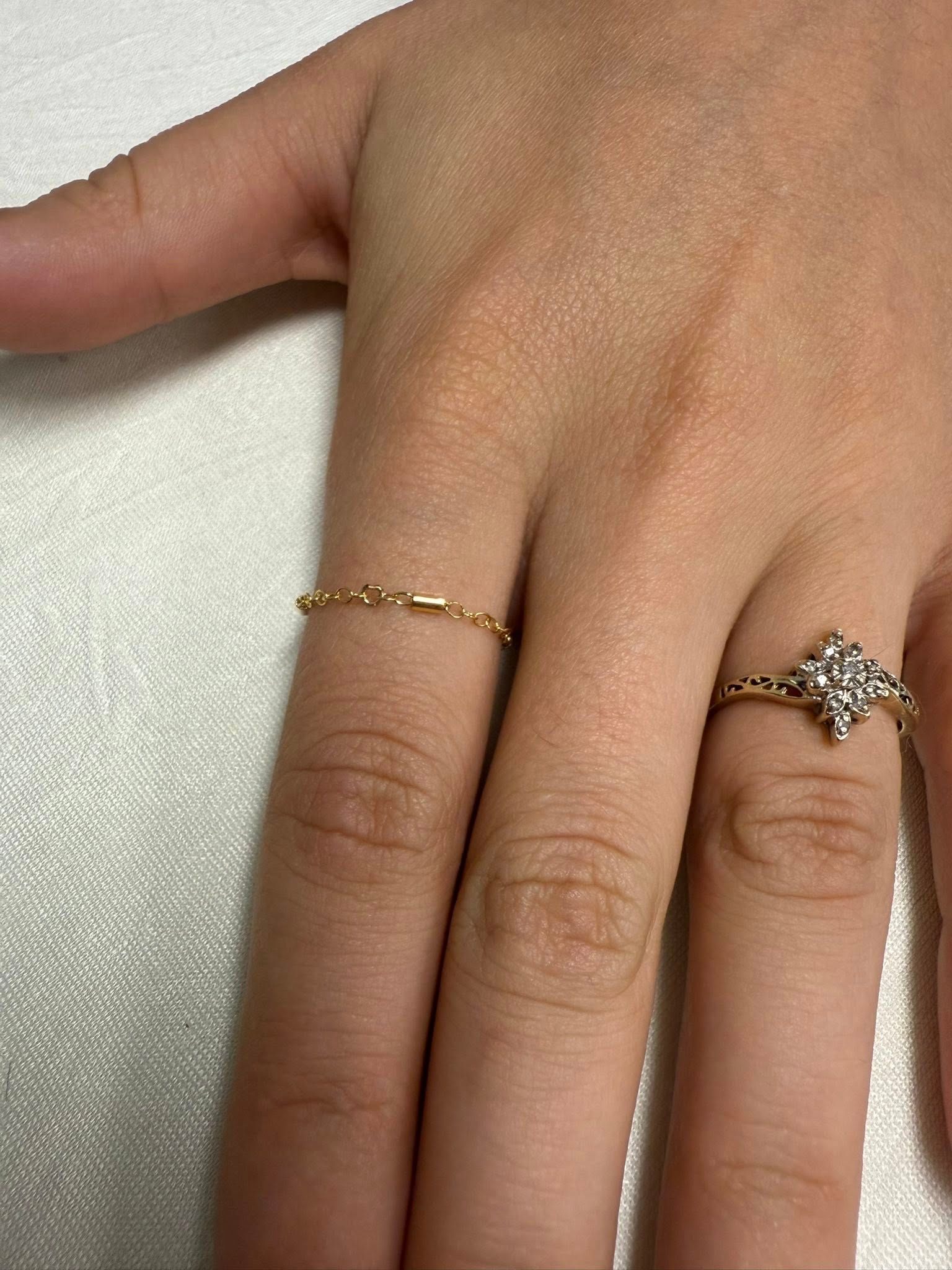 Hand with thin gold and silver star rings resting on a light fabric background