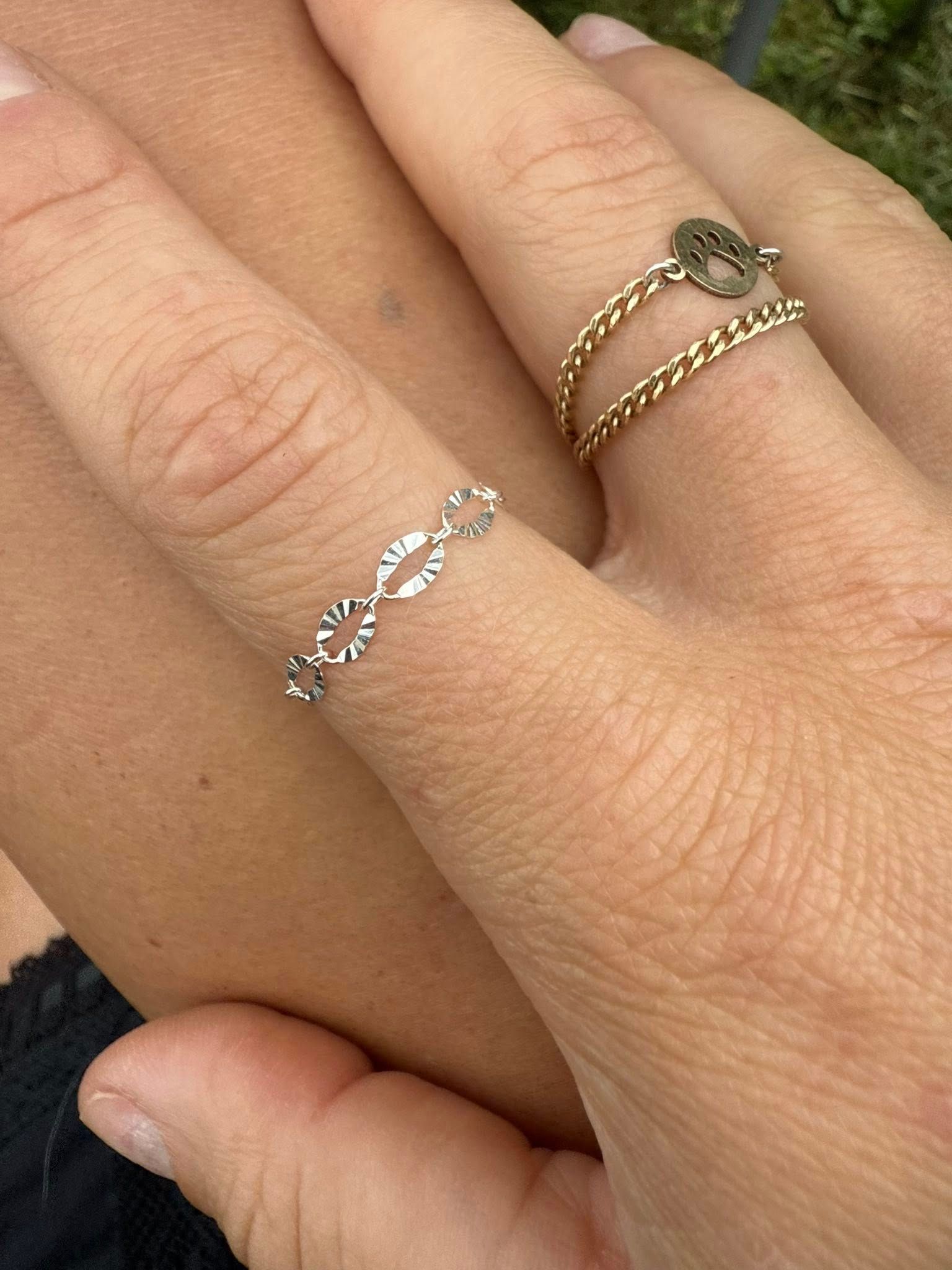 Two hands clasped, wearing delicate silver and gold rings with heart designs